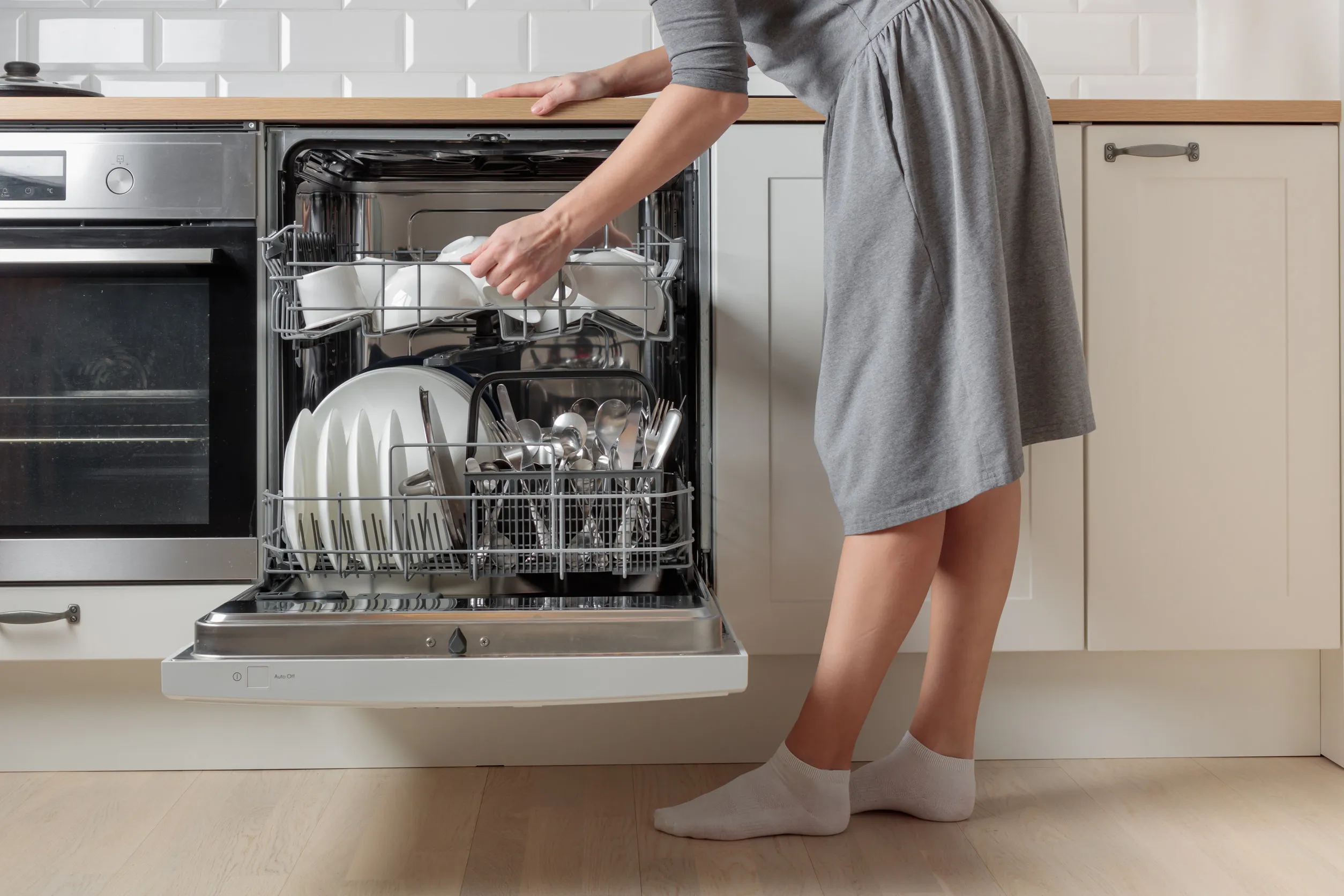 thumbnail - 하얀색 주방에서 붙박이 식기세척기를 여는 여성. 내부에는 세척이 완료된 접시와 식기가 가지런히 놓여 있다. 시간 절약형 주방가전의 한 장면. 출처=123rf