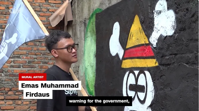 thumbnail - 인도네시아 벽화가 에마스 무함마드 피르다우스가 ‘원피스’ 속 밀짚모자 해적단 깃발을 그린 졸리 로저 벽화를 완성하고 있다. 그는 ‘정부에 대한 경고의 상징’이라고 설명했다.  CNN 캡처