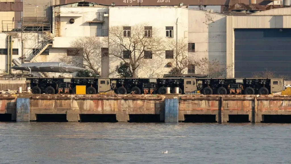 thumbnail - 중국 상하이 후둥-중화 조선소 부두에서 트럭형 전자기 사출기 모듈이 열차처럼 연결된 모습. 앞서 육상에서 포착된 이동식 전자기 사출 체계와 구조적으로 동일한 형태로, 여러 대의 차량이 하나의 연속된 사출 궤도를 이루고 있다. 인근에는 임시 수상 전투함으로 개조된 화물선이 정박해 있었다. 중국 인터넷 캡처