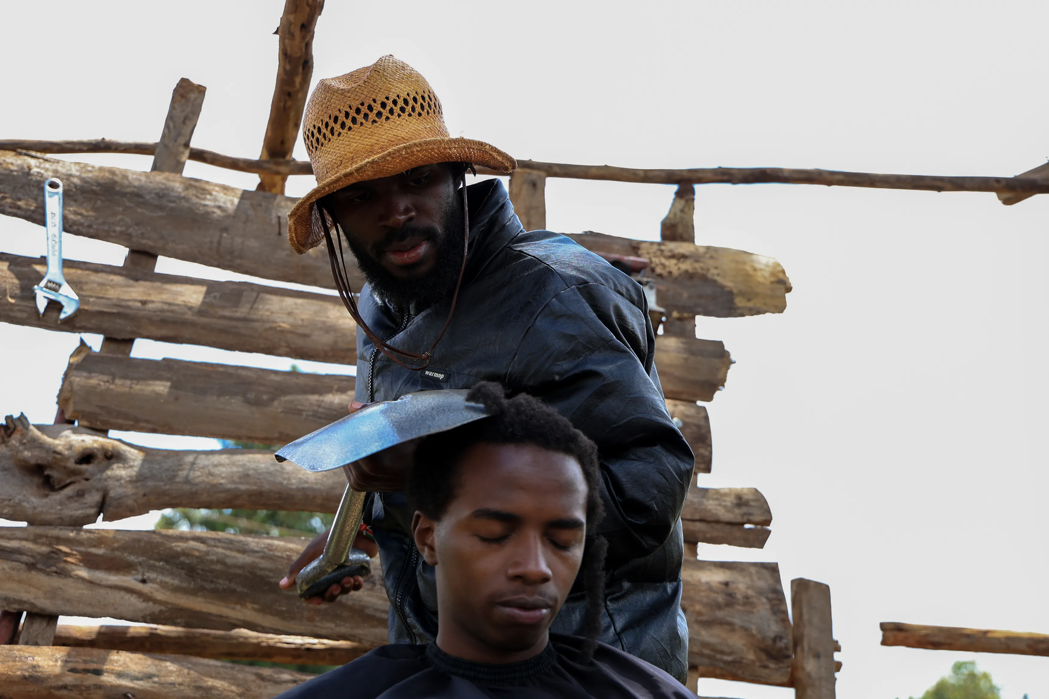 thumbnail - 케냐 키암부 지역에서 이색적인 도구를 활용한 이발 영상으로 유명한 이발사 사파리 마틴스가 삽을 이용해 이안 은젠가의 머리를 손질하고 있다. 2025.11.26. AP 연합뉴스