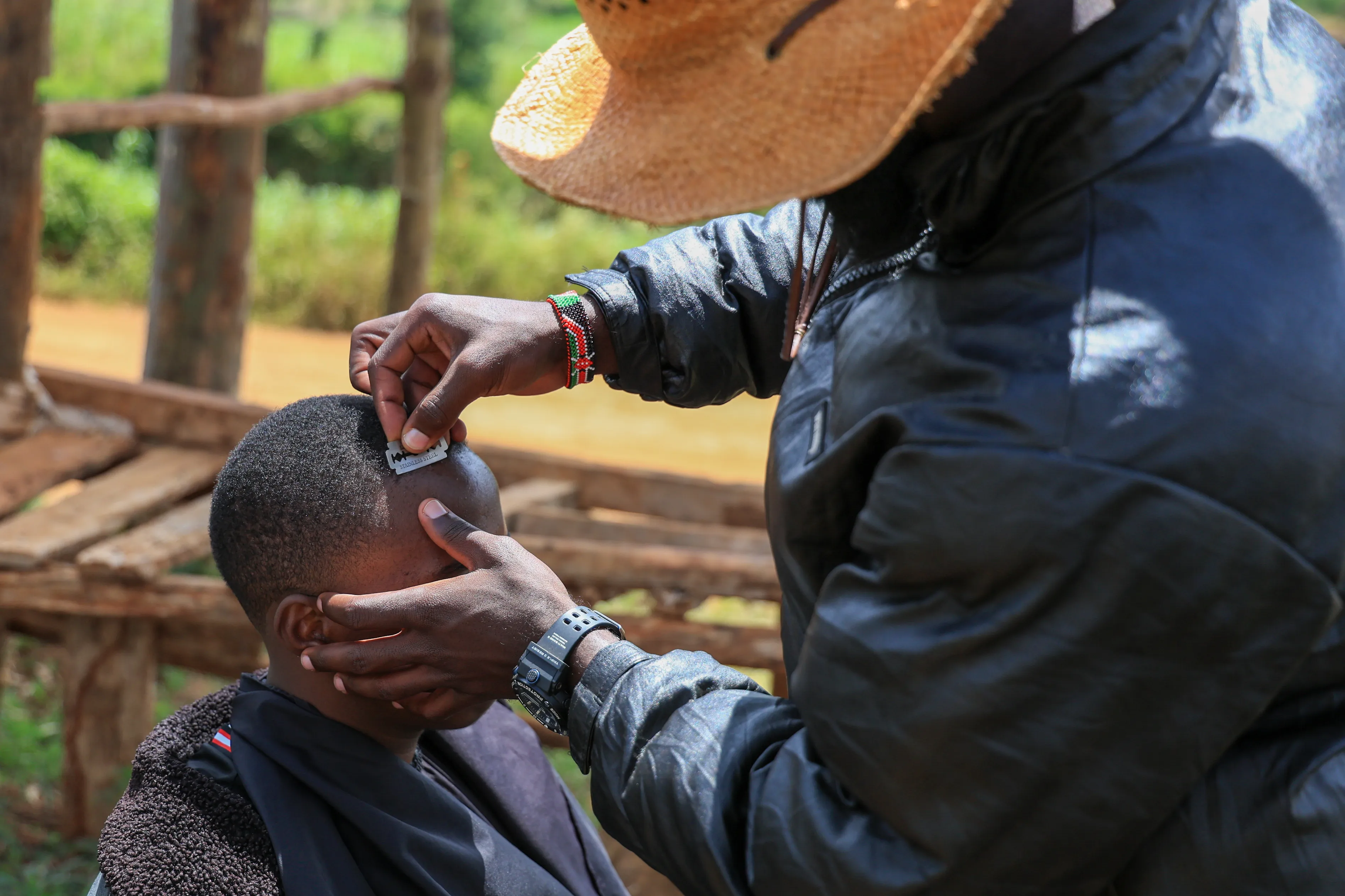 thumbnail - 케냐 키암부 지역에서 온라인상에서 이색적인 이발 방식으로 알려진 이발사 사파리 마틴스가 면도날을 이용해 이안 은젠가의 머리를 손질하고 있다. 2025.11.26. AP 연합뉴스