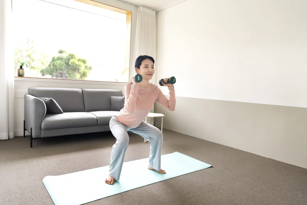 thumbnail - 집에서 가벼운 덤벨을 들고 스쿼트 동작을 하는 모습. 연구에 따르면 무거운 중량이 아니어도 근육이 지칠 때까지 반복하면 근력 향상을 기대할 수 있다. 아이클릭아트