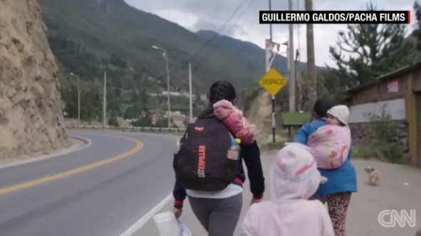 가방을 맨 채 도롯가를 걷고 있는 페루 여성 탐보 일가족