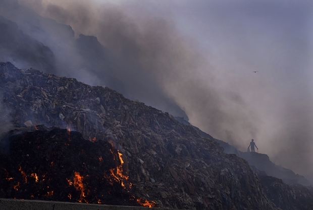 27일(현지시간) 인도 수도 뉴델리 발스와 쓰레기 매립지 화재 현장 저 멀리 쓸만한 쓰레기를 고르는 폐기물 수집가가 보인다./로이터 연합뉴스