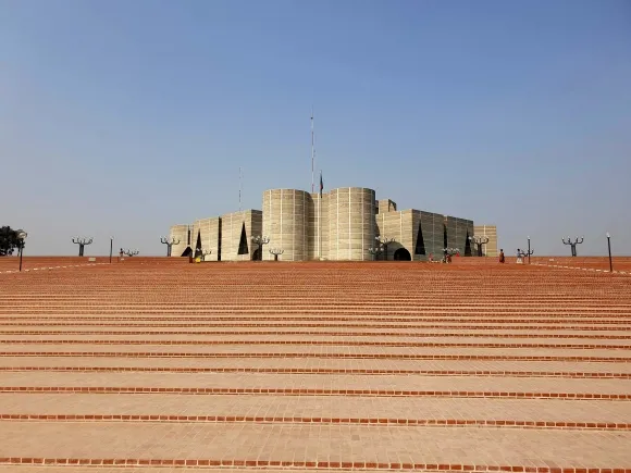 정문을 통과하여 남측에서 바라본  방글라데시 다카 국회의사당 전경. 남측 상공에서 바라보면 팔각형의 정확한 각도를 유지한 평면이다. 하지만 유일하게 남측 주통로의 축이 비스듬히 기울어진 이유는 정북방향을 맞추기 위해서라고 한다.
