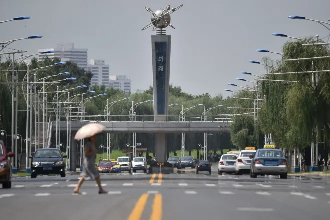 2024년 8월 13일 북한 평양 미래과학자거리에서 한 주민이 강한 햇볕을 가리기 위해 우산을 쓴 채 길을 건너고 있다. AFP 연합뉴스