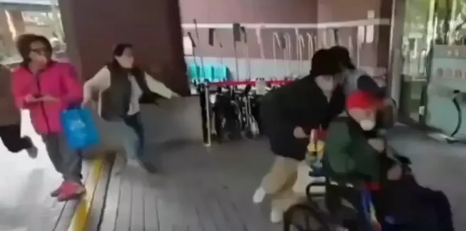 병원 출구에서 가족들이 102세 왕 씨의 휠체어를 밀어 이동시키는 가운데, 검은색 조끼를 입은 간병인이 뒤에서 이를 따라오고 있다.