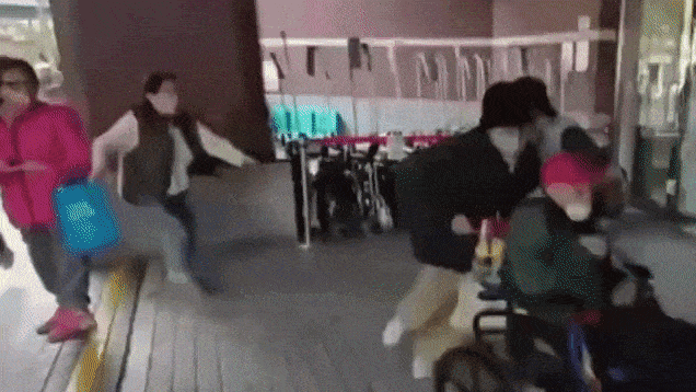 병원 출구에서 가족이 102세 왕 씨의 휠체어를 밀어 이동시키는 가운데, 검은색 조끼 차림의 간병인이 뒤에서 황급히 따라붙고 있다.