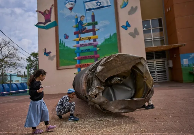 이란의 미사일 공격 이후 23일(현지시간) 요르단강 서안 페두엘 정착촌의 한 학교 운동장에 떨어진 탄도미사일 잔해 옆에서 아이들이 주변을 살피고 있다. AP 연합뉴스